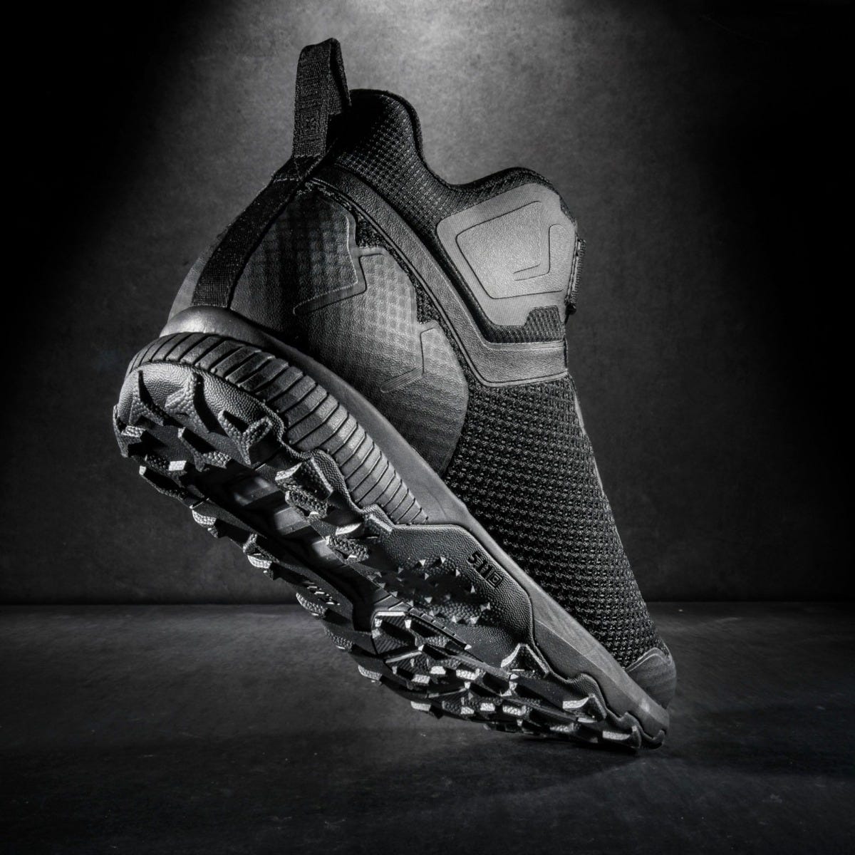 Black athletic shoe with textured sole on a dark background