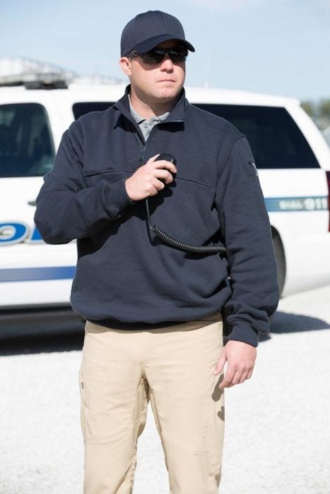 Person wearing a navy jacket and beige pants standing in front of a white vehicle.