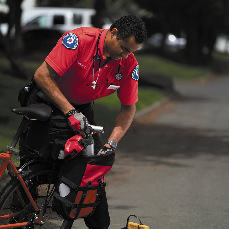 Person in a red uniform with medical insignia attending to a bicycle on a street.