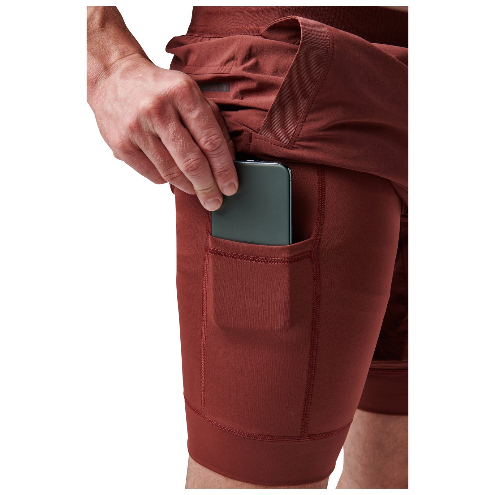 Person wearing red shorts with a pocket holding a smartphone on a white background