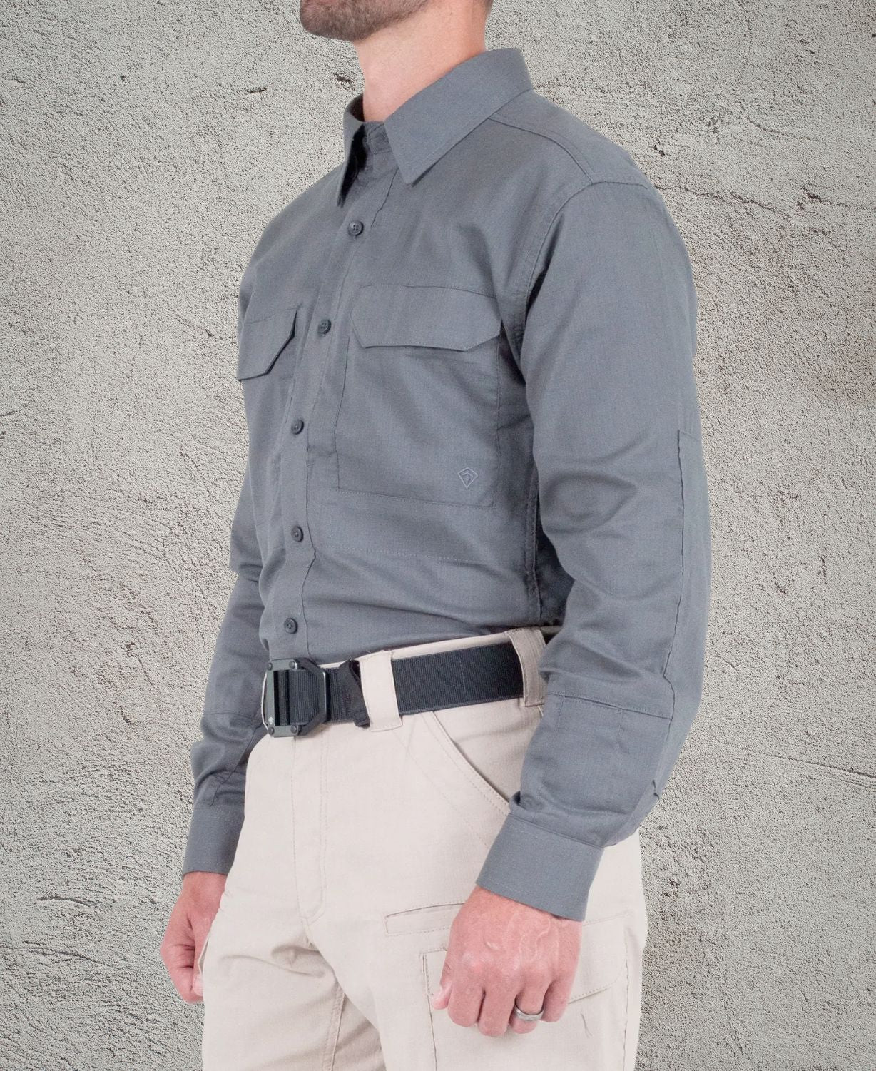 Person wearing a gray shirt and beige pants against a textured wall.