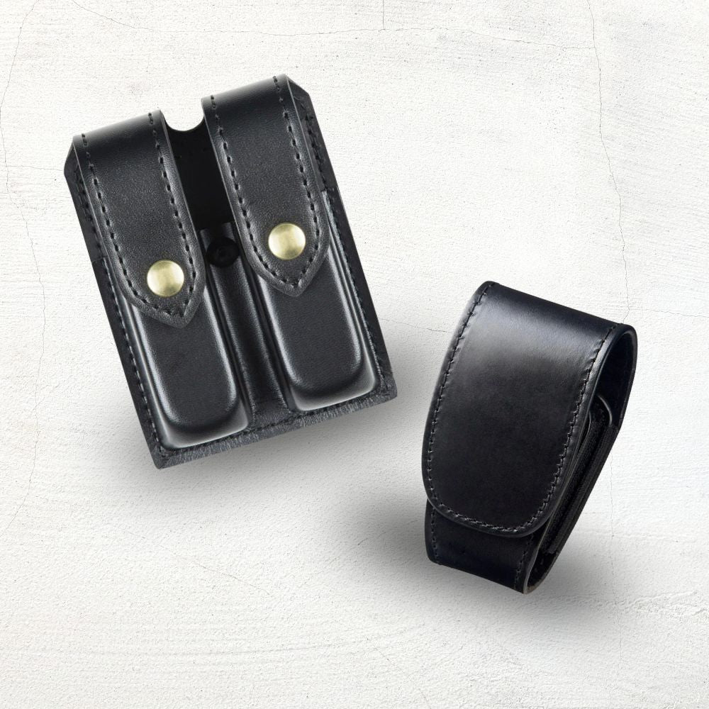 Two black leather pouches with brass fasteners on a beige background